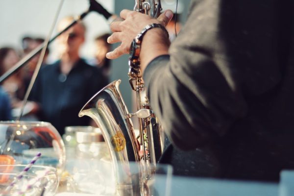 A saxophonist playing music at an event with an audience in the background.