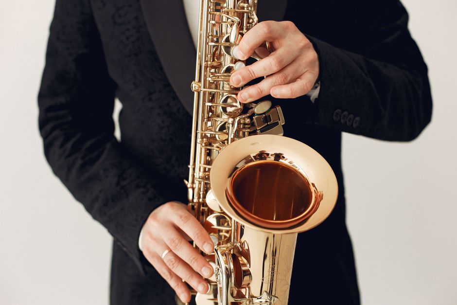 Unrecognizable talented male musician wearing concert costume playing jazz melody on saxophone standing against white background during music show or live entertainment