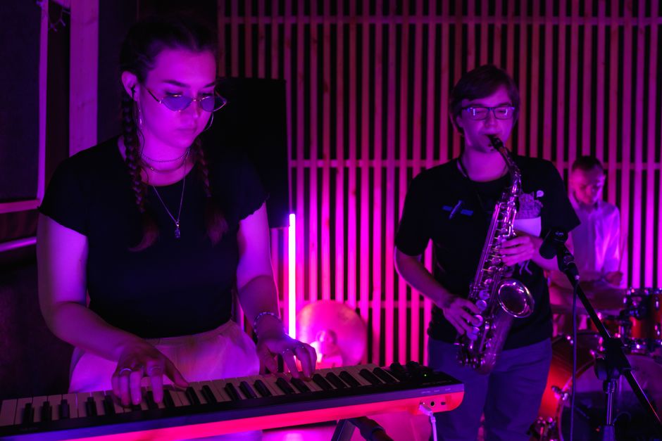 A band performing live music with a keyboard and saxophone under colorful stage lighting.