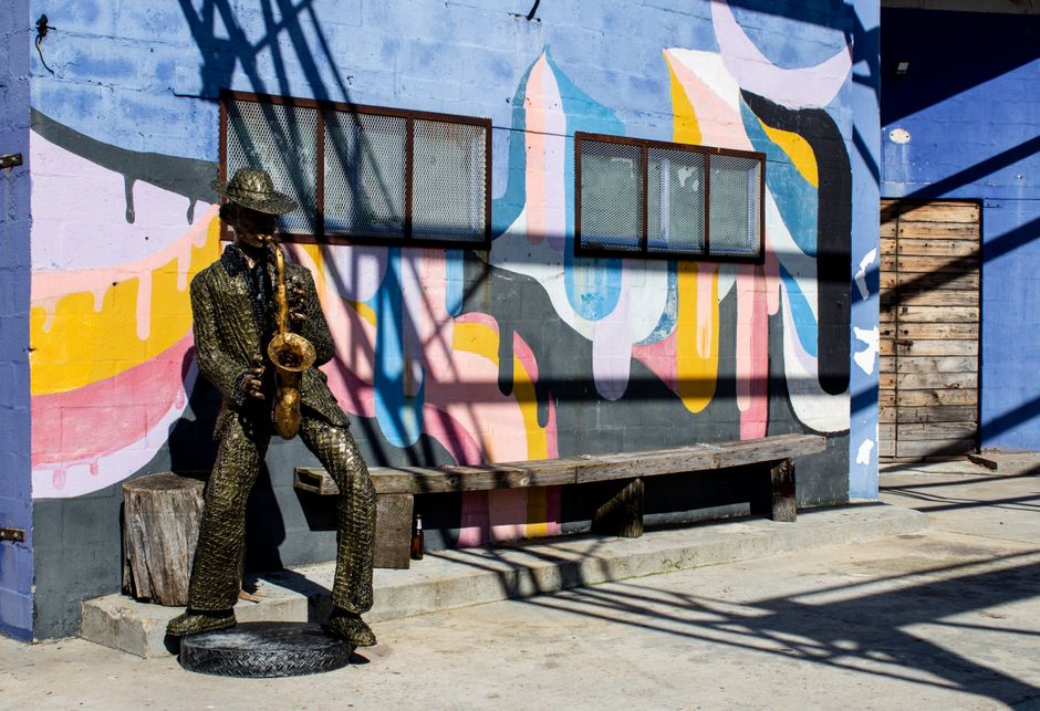Metal saxophonist statue in front of vibrant street art mural under sunlight.