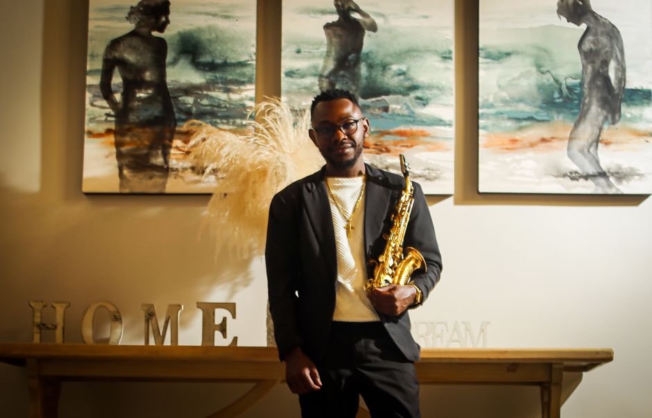 A stylish man with a saxophone stands in a modern art-filled home in South Africa.