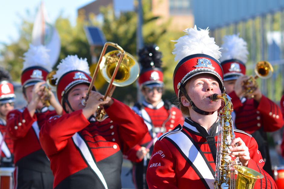 Energetic marching band in red uniforms playing brass instruments outdoors during the day.