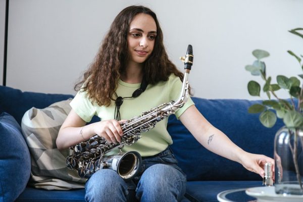 Young woman enjoying music with saxophone, sitting on a blue sofa indoors.