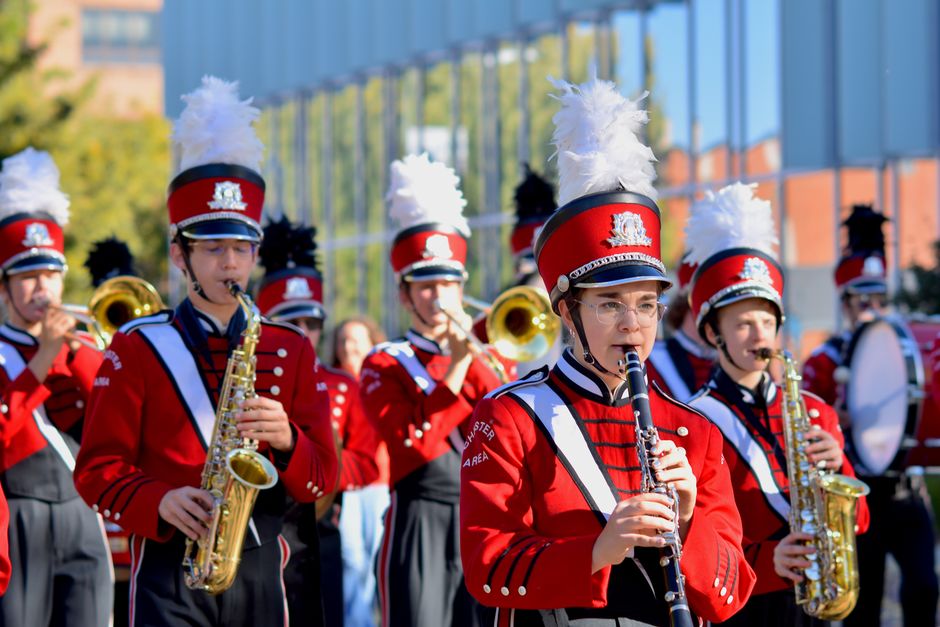 Colorful marching band playing instruments at an outdoor event in bright sunlight.