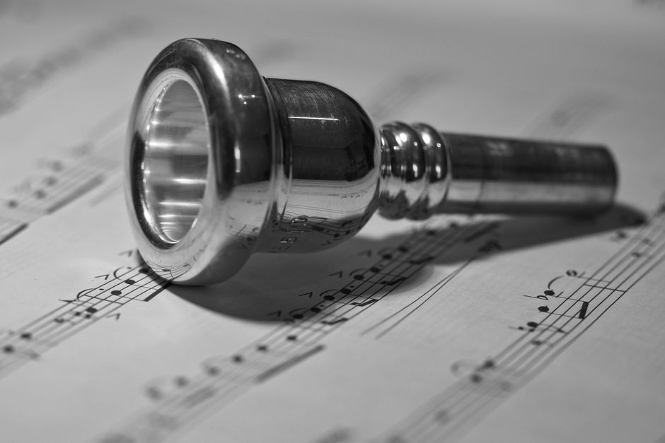 A detailed black and white image of a brass mouthpiece resting on sheet music, highlighting its polished texture.