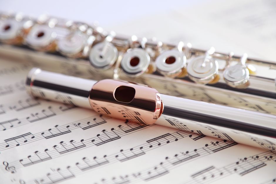 Detailed view of a silver flute resting on music sheets, showcasing artistry and craftsmanship.