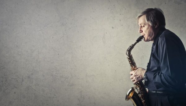 Elderly man passionately plays saxophone against a textured wall. Side profile.