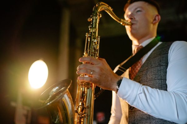A young male saxophonist playing under warm stage lights indoors.