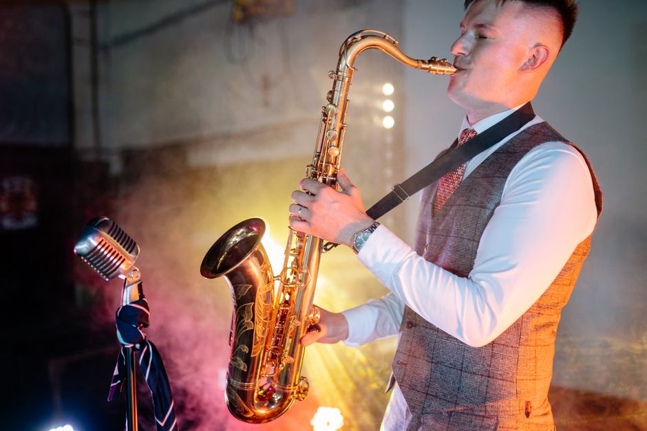 An adult male musician plays the saxophone passionately in an indoor jazz setting.