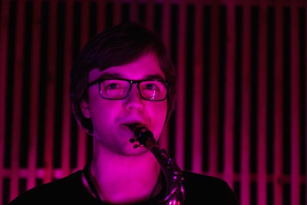 A saxophonist playing indoors with vibrant pink lighting creating a dramatic atmosphere.