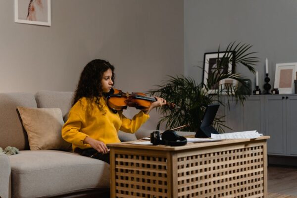 A girl in yellow sweater practicing violin in a warm home setting.
