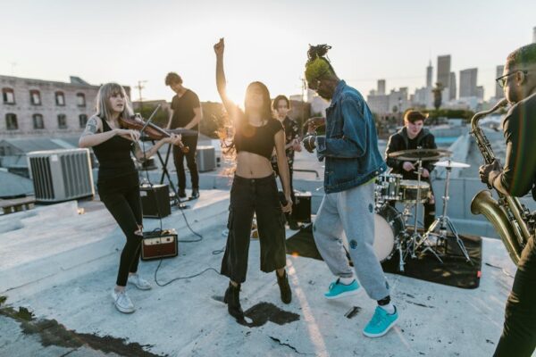 A diverse group of musicians perform energetically on a rooftop at sunset.