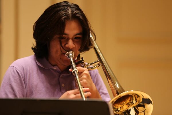 Close-up of a young man playing a trombone indoors, focusing intensely.