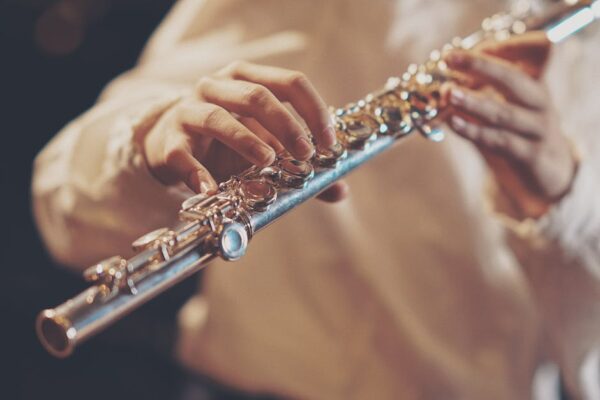 Focused image of a musician's hands playing a silver flute during a performance.