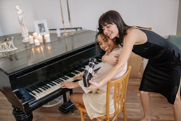 Two women joyfully embracing while capturing a moment by the piano, showcasing friendship and happiness.