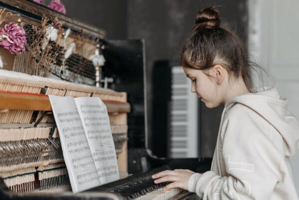 A young girl practicing piano with sheet music in an indoor setting, focused and engaged.