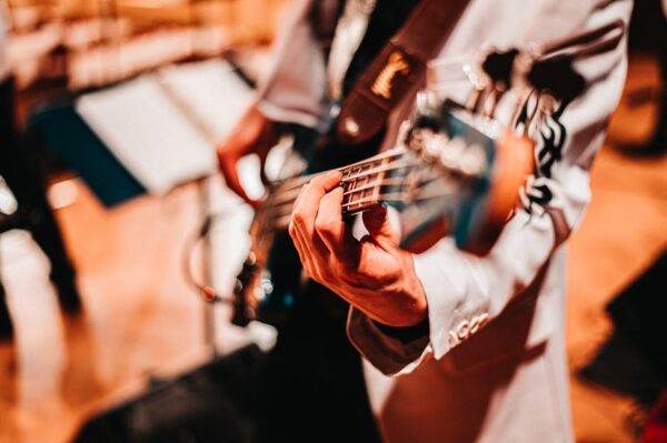 Close-up of a musician playing a bass guitar with a blurred background, warm tones.