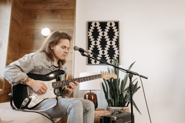 Young caucasian man playing electric guitar indoors with microphone setup.
