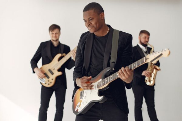 Three musicians performing energetically with guitar, saxophone, and bass indoors.