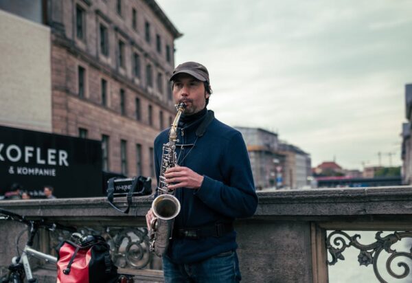 A street musician playing a saxophone on a city bridge, surrounded by urban architecture.