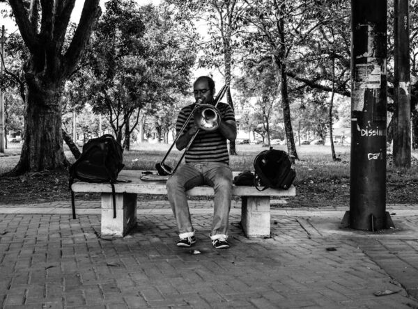 Black and white photo of a street performer playing the trombone on a park bench in Campinas, Brazil.