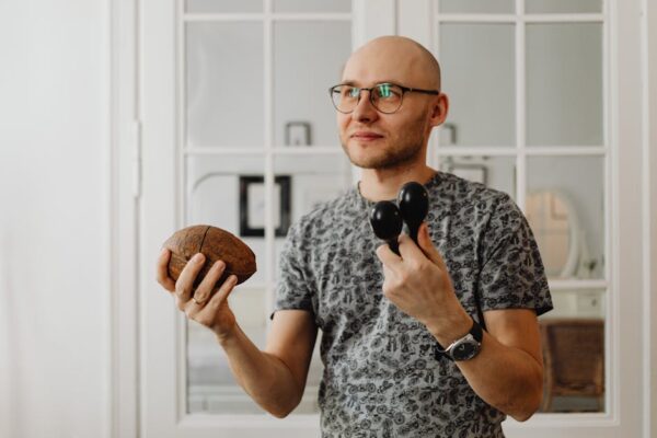 Bald man with eyeglasses holding maracas and coconut shell indoors.