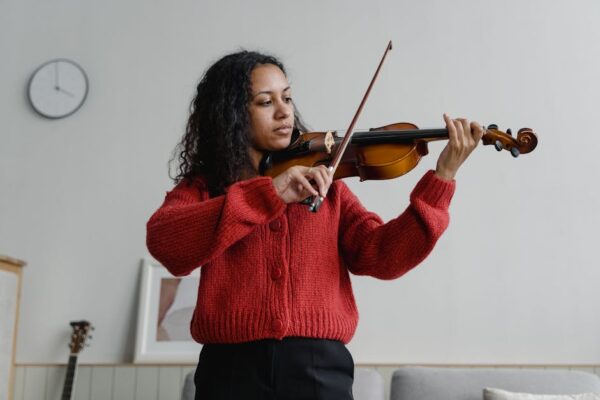 Woman in a red sweater playing violin indoors, showcasing talent and concentration.