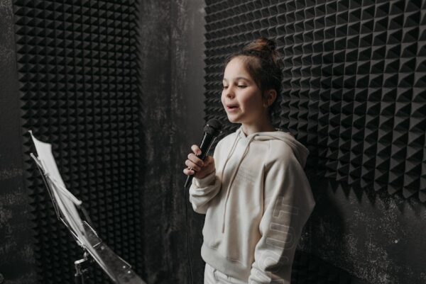 A young girl sings into a microphone in a soundproof room with acoustic panels around her.