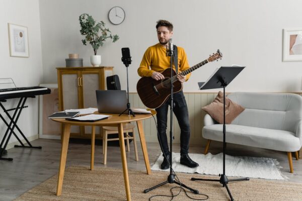 Man playing acoustic guitar during music practice session indoors, with music equipment.