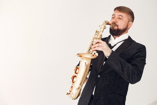 Stylish man in a suit playing saxophone with passion against neutral background.