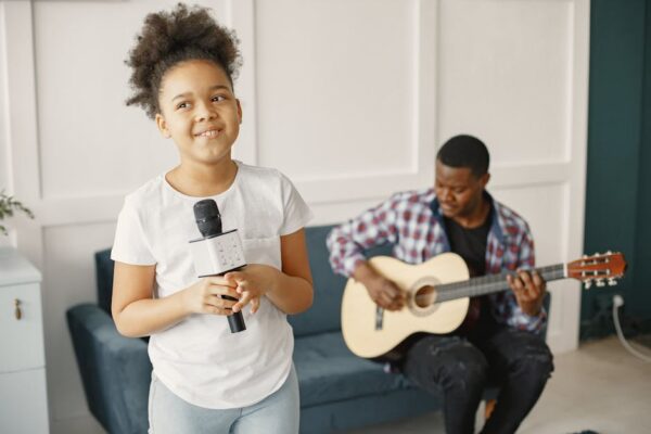 Father playing guitar as daughter sings joyfully with a microphone indoors.
