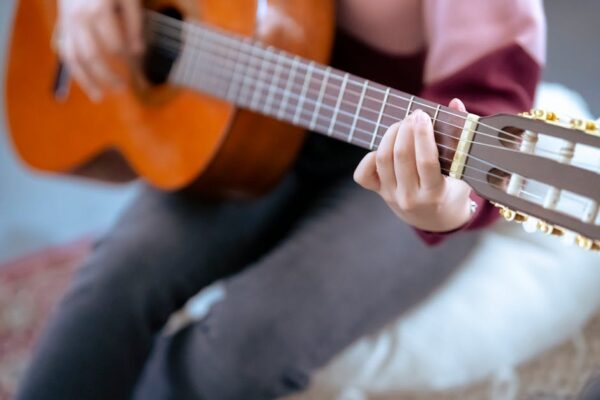 Soft focus of crop anonymous female musician in casual outfit playing acoustic guitar while sitting on pouf