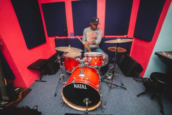 A drummer rehearses on a red drum set in a colorful recording studio in Trinidad and Tobago.