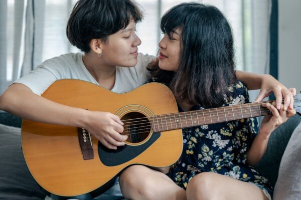 A loving couple shares a tender moment while playing guitar together indoors.