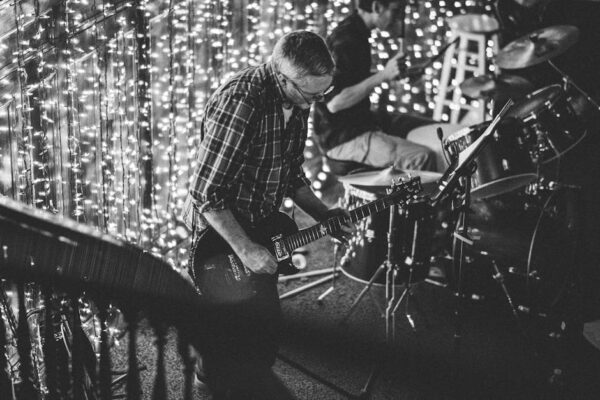 Black and white image of a live music performance featuring a guitarist and drummer.