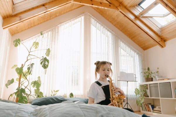 A young girl plays the saxophone in a bright, airy room filled with plants, creating a serene musical setting.