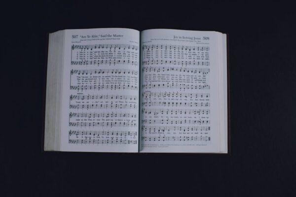 An open hymn book displaying musical notes and lyrics on a black background.