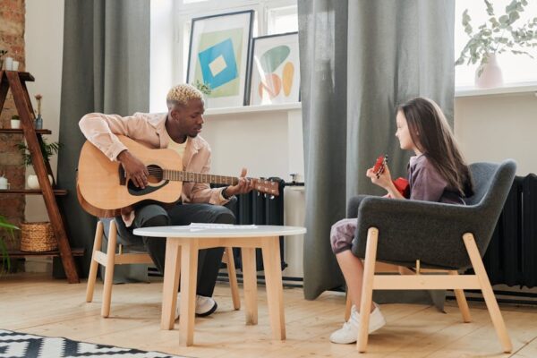 A man teaches a girl guitar in a cozy living room setting during daytime.