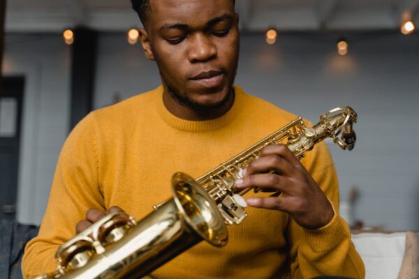 Young black male saxophonist playing indoors, wearing a yellow sweater.