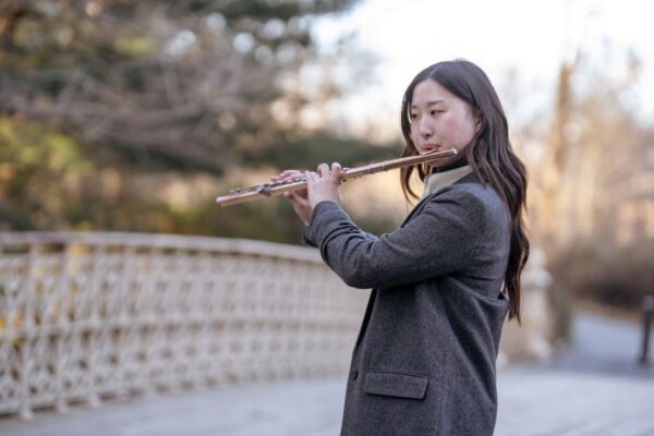 Elegant young woman playing the flute on a peaceful autumn day outdoors.
