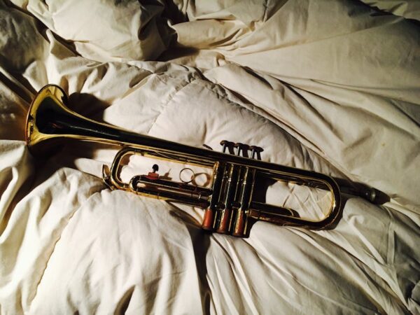 A classic brass trumpet resting on a soft, textured white comforter, illuminated by warm natural light.