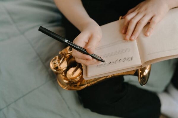 A musician writing handwritten sheet music on a notebook resting on a saxophone.