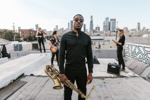 Musicians performing on a rooftop with a saxophonist in focus and city skyline in the background.