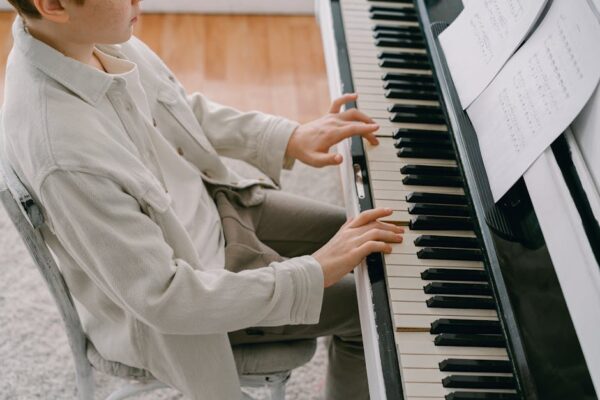 A young person playing piano with a music sheet, focusing on the keys and hands.