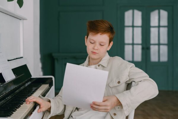 A young child reading sheet music while sitting at a piano indoors, focusing on practice.