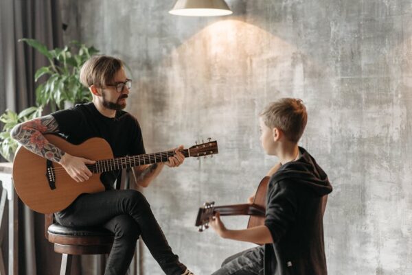 A man teaching a boy to play the acoustic guitar in an indoor setting.
