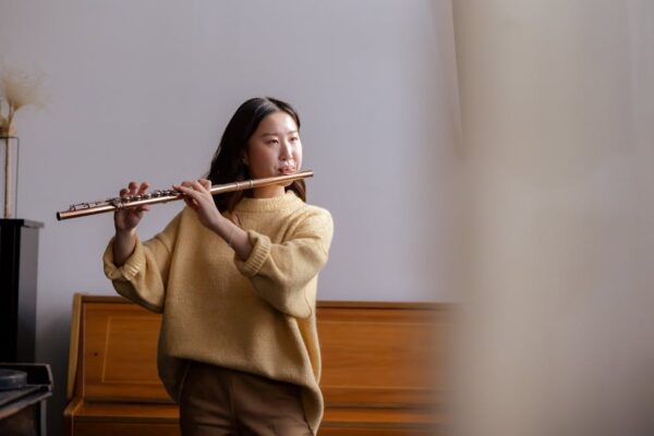 Young Asian woman plays the flute in an indoor setting, focusing on music practice and creativity.