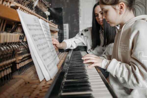 A child learning to play piano with guidance from an adult in a cozy setting, focusing on music sheets.