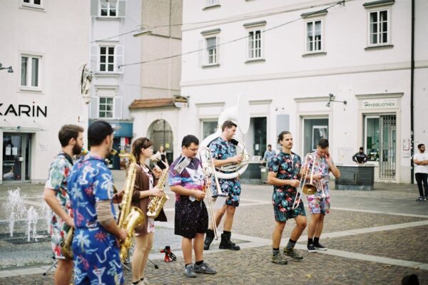 A lively street band performing with brass instruments on a city square, showcasing colorful outfits.