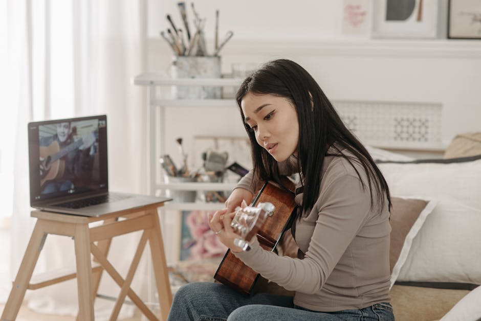 Asian woman taking an online guitar lesson at home using a laptop.